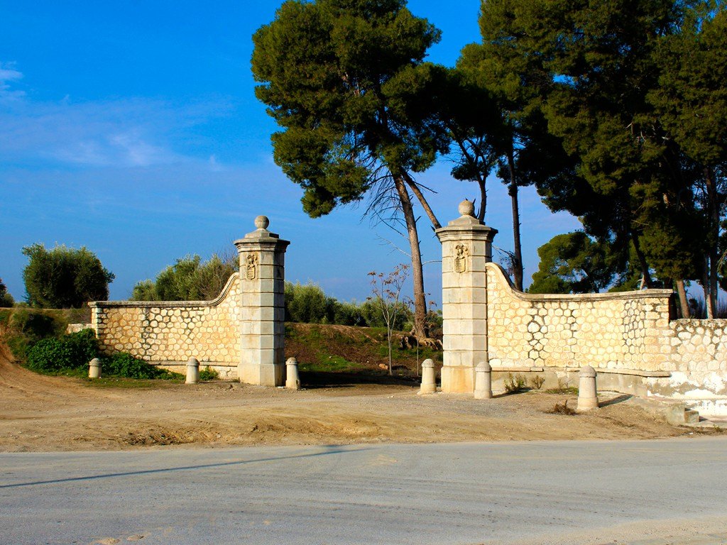 La Portada de Trasmulas: dos pilares de piedra junto a un muro, con pinos y cielo azul